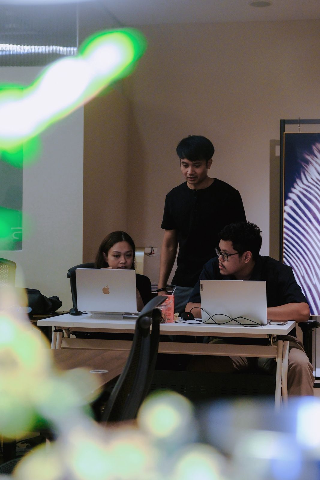 An instructor standing beside two learners as they work on their laptops