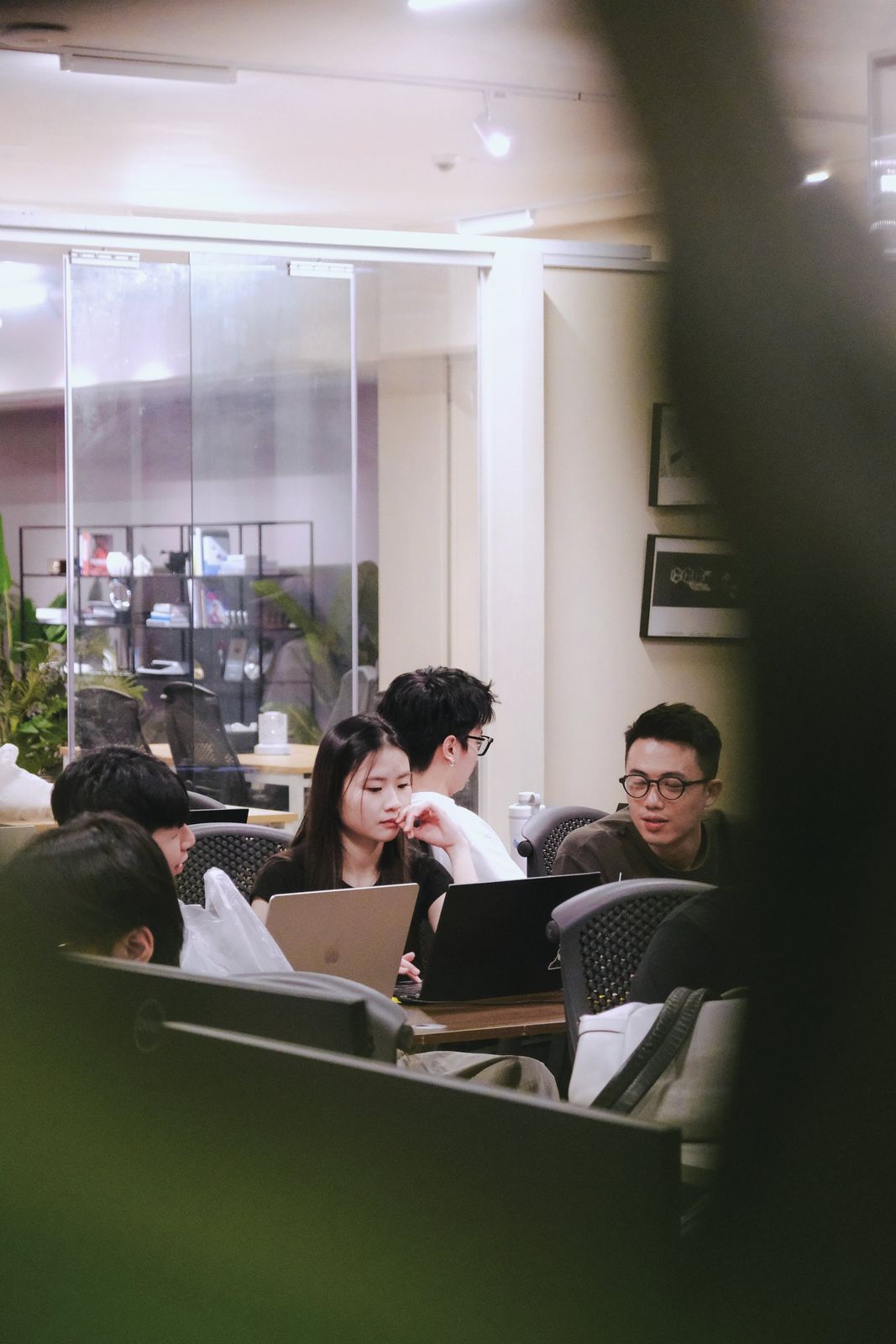 Learners working on laptops around a classroom table, seen through a doorway