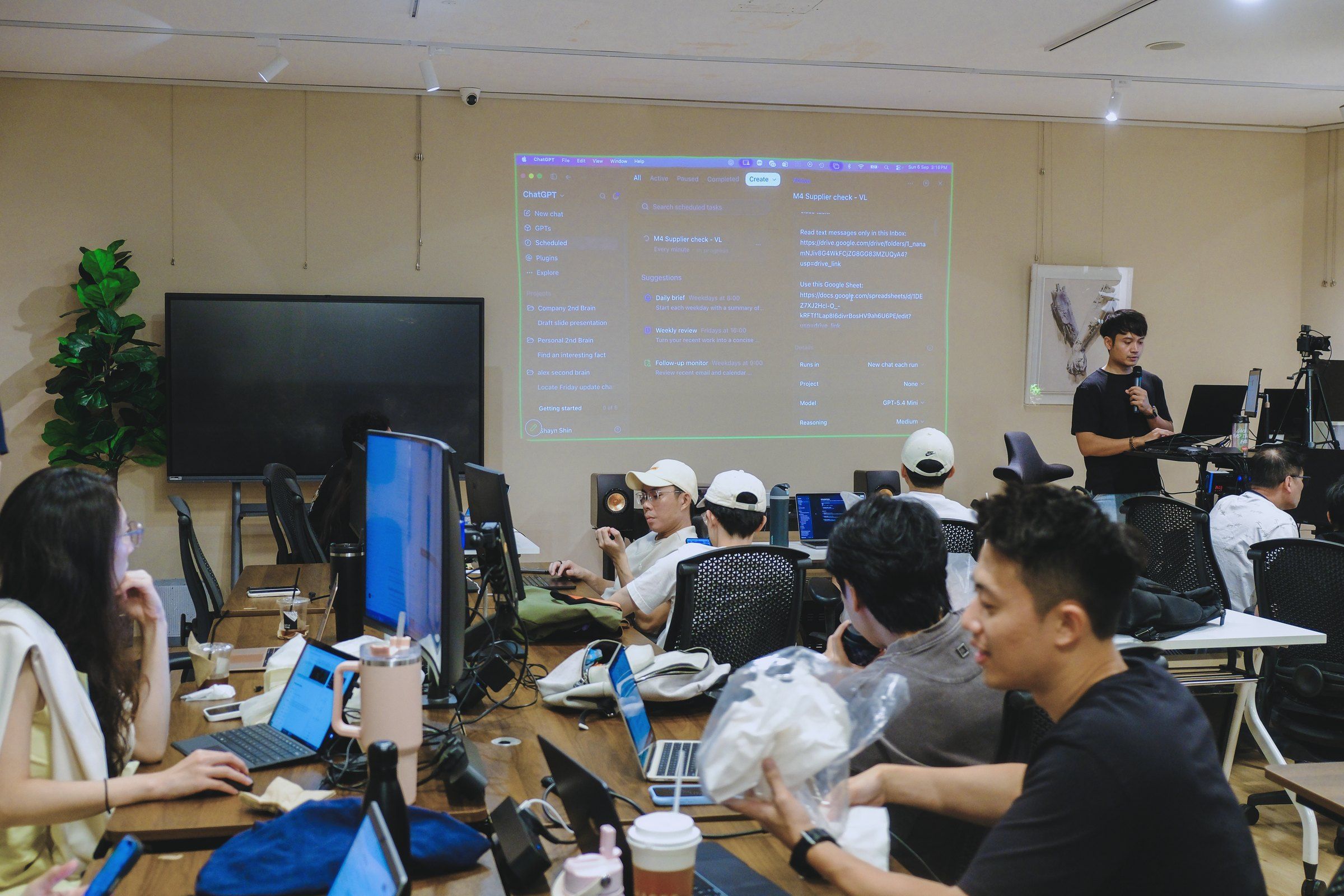 An instructor with a microphone presenting a ChatGPT workflow to a full classroom of learners at their screens