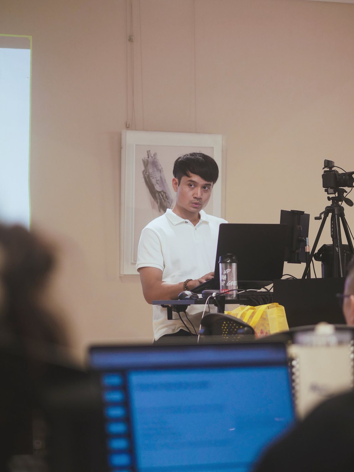 An instructor teaching from a laptop at the front of the class, seen past learners' screens